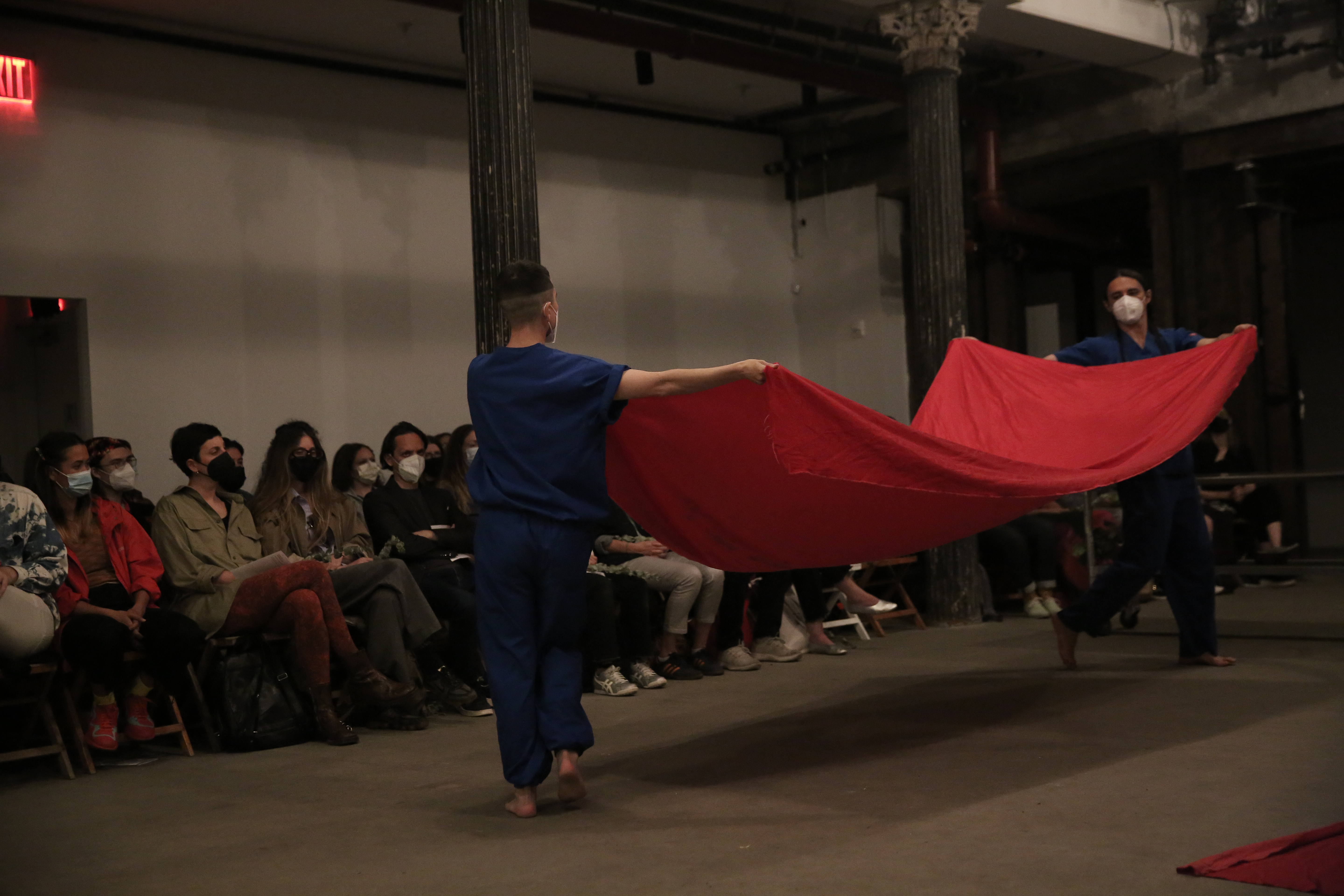 Two figures wearing medical scrubs suspend a piece of red fabric between themselves.