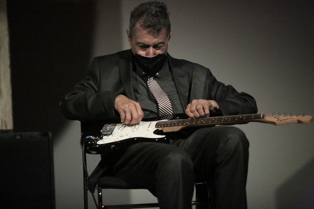 A seated figure plays a guitar that lies in his lap.