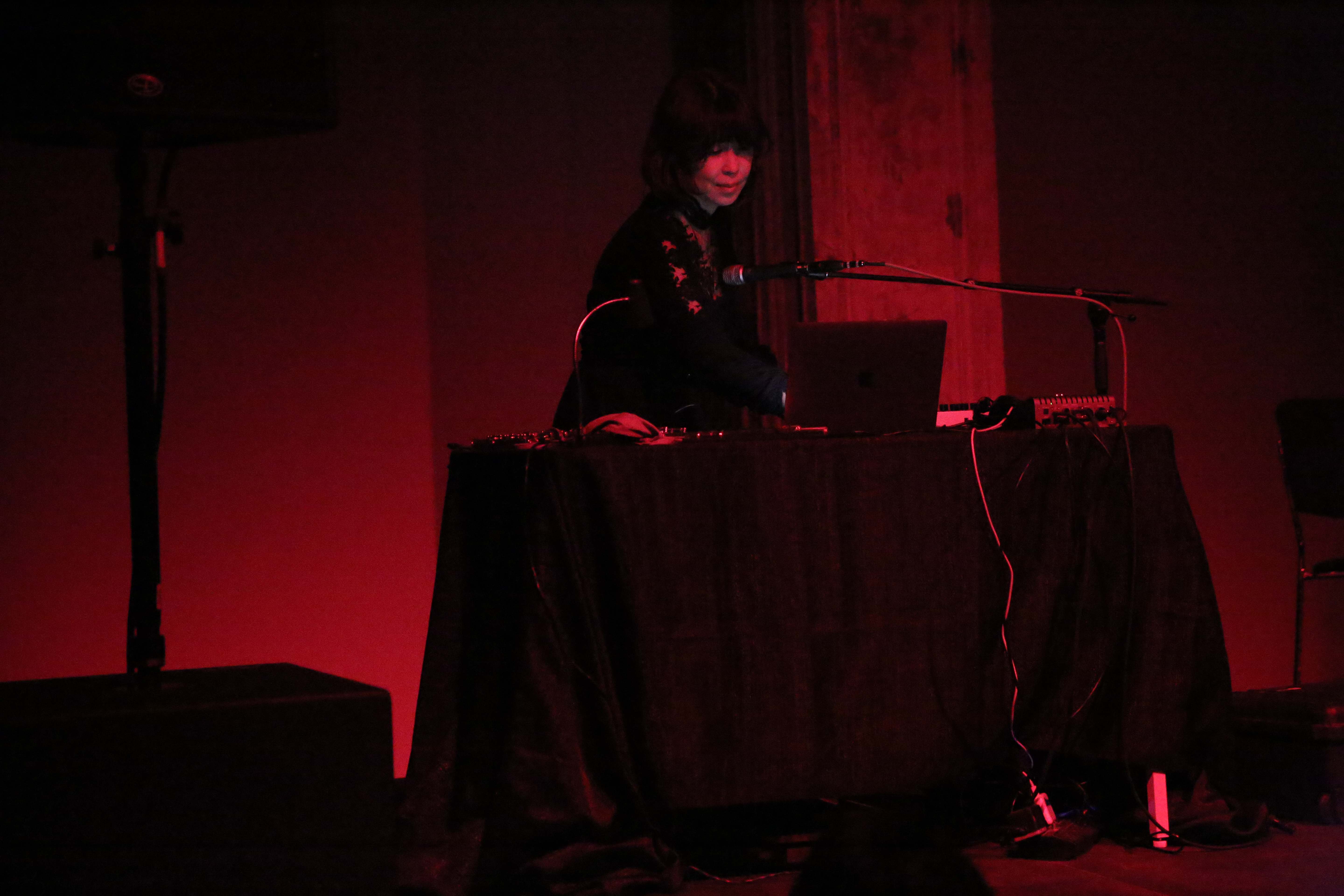 A figure illuminated by red light stands behind a table, using a computer that sits on the table.