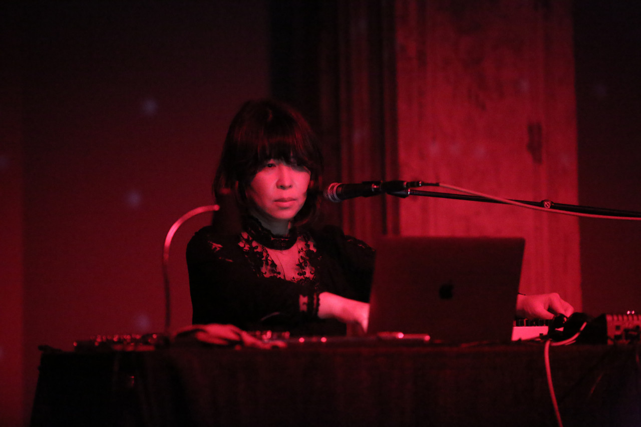 A figure in front of a microphone looks down upon a computer.