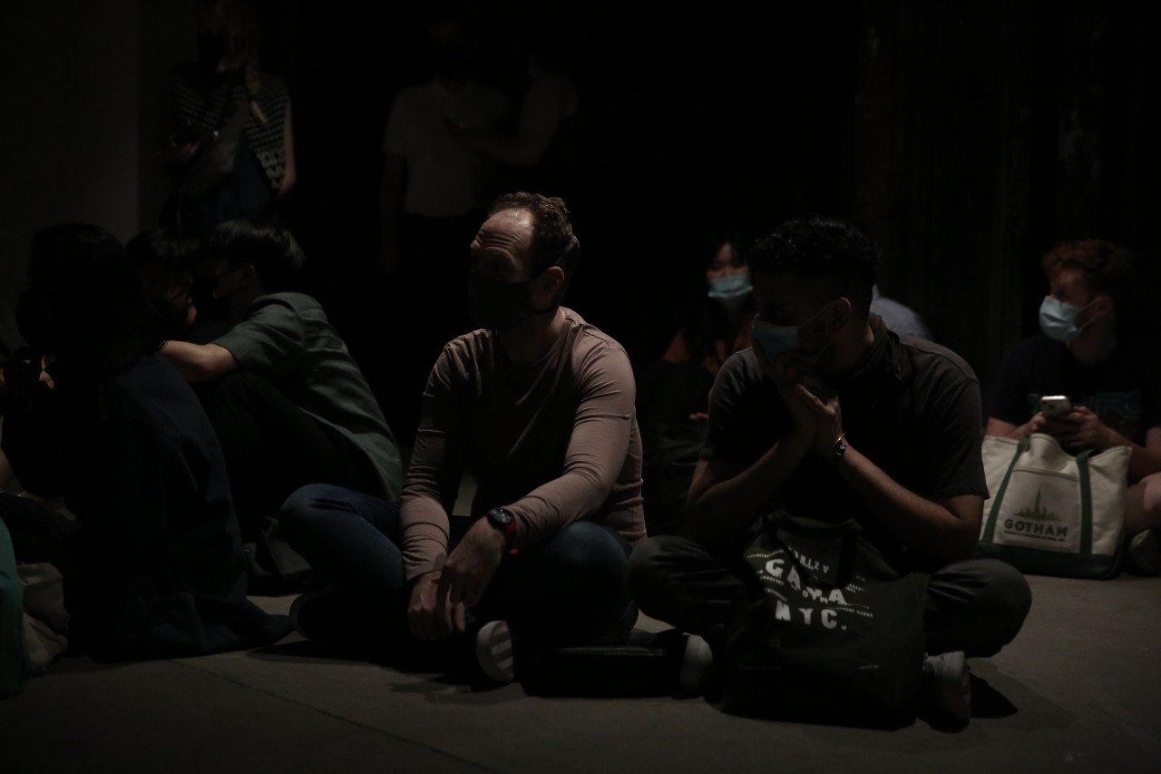 Several figures sit on the ground, legs crossed.