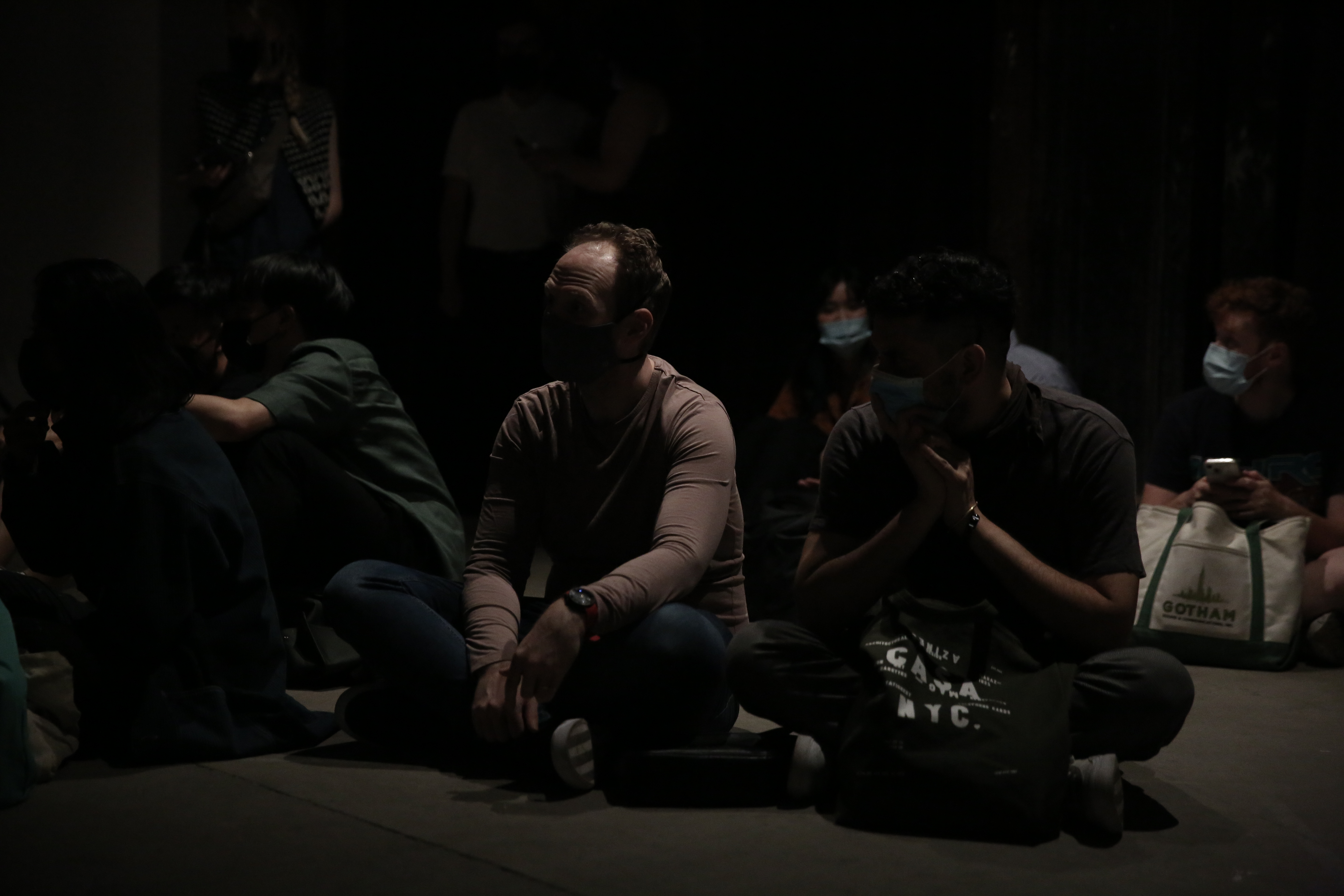 Several figures sit on the ground, legs crossed.