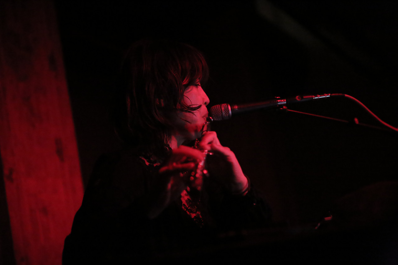 The upper body of a figure appears in front of a microphone, into which they play the flute.