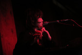 The upper body of a figure appears in front of a microphone, into which they play the flute.