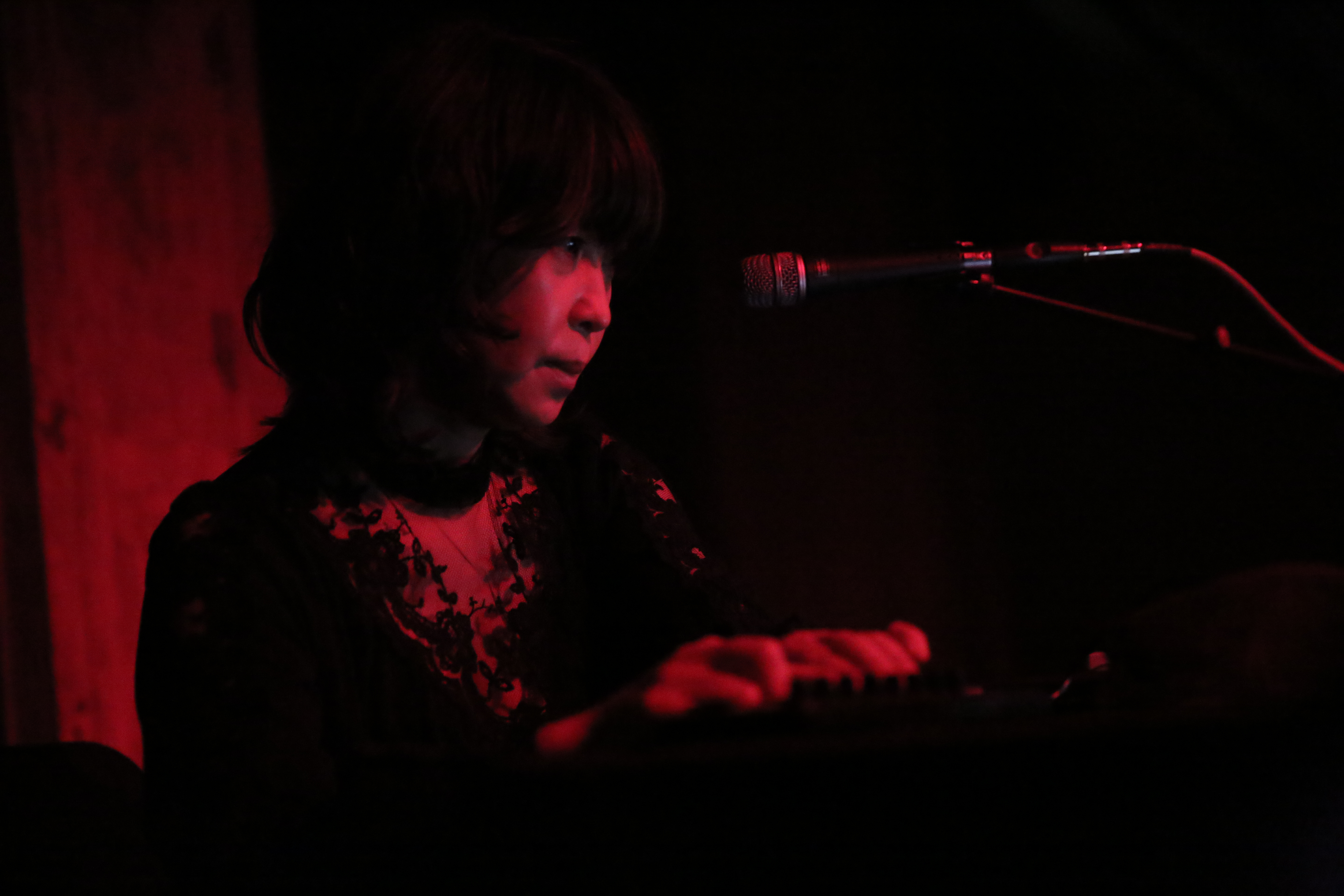 A figure faces towards a microphone and red light, playing some sort of instrument that is out of focus.