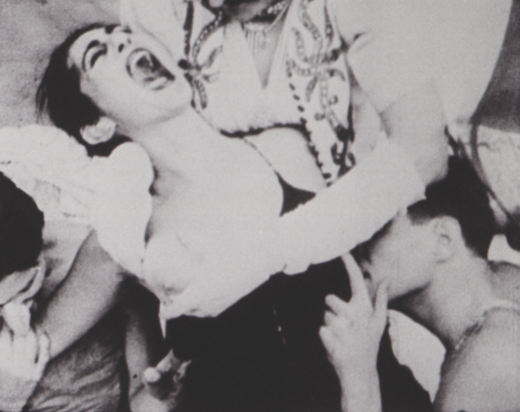A woman screaming while two men hold her down and touch her breasts.