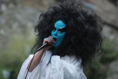 A person with their face painted blue, framed by a large black mane of hair.