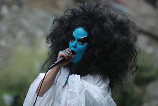 A person with their face painted blue, framed by a large black mane of hair.