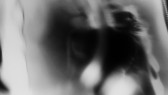 A black-and-white film still of hazy and ghostly tonal modulations. Within the tonal atmosphere, fragments of a person's face and body can be made out in the right half of the image.