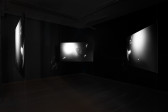 A color documentation image of Shala Miller's Genesis, 2023. Three monochrome projection panels float equidistantly in a dark room, with vinyls on blacks walls.