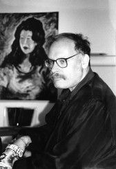 A profile of a man wearing glasses gazing beyond the frame. He sits in front of a painted portrait of a figure, who gazes in the same direction.