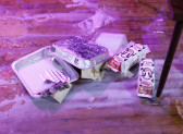 Several empty food containers and milk boxes on a hardwood floor, with milk spilled out all over the floor.