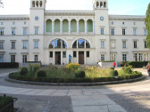 The façade of a large, stone museum. A cobblestone, roundabout path snakes in front of the museum, with a series of bushes and greenery planted in the middle of the roundabout.