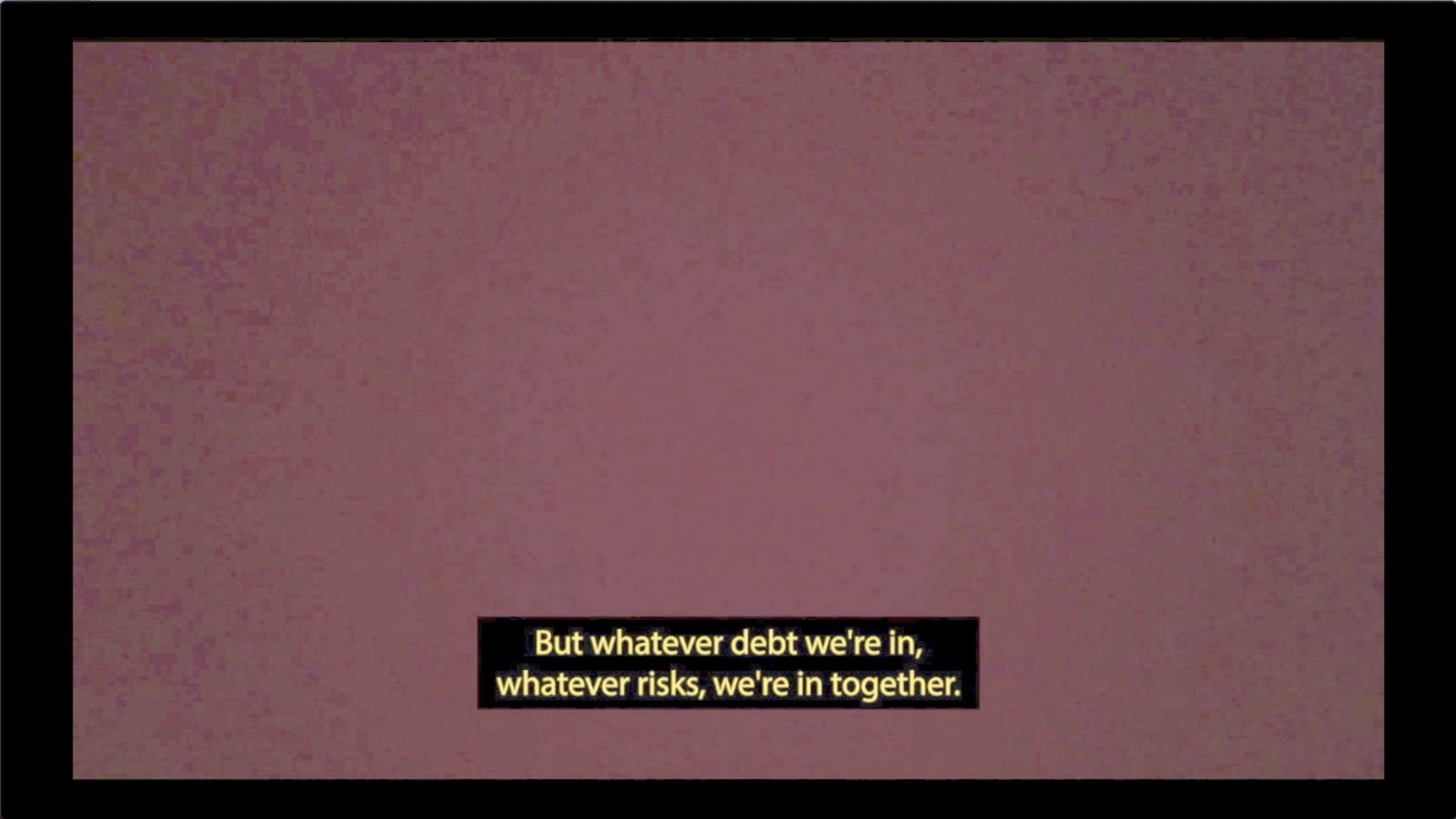 In front of a pixelated red background, a yellow caption appears on top of a black bar that reads: “But whatever debt we’re in, whatever risks, we’re in together.