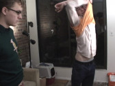One man takes off an orange sweater while another man watches.