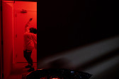 Color photograph of a figure dressed in all white, dancing in a corridor bathed in red light.