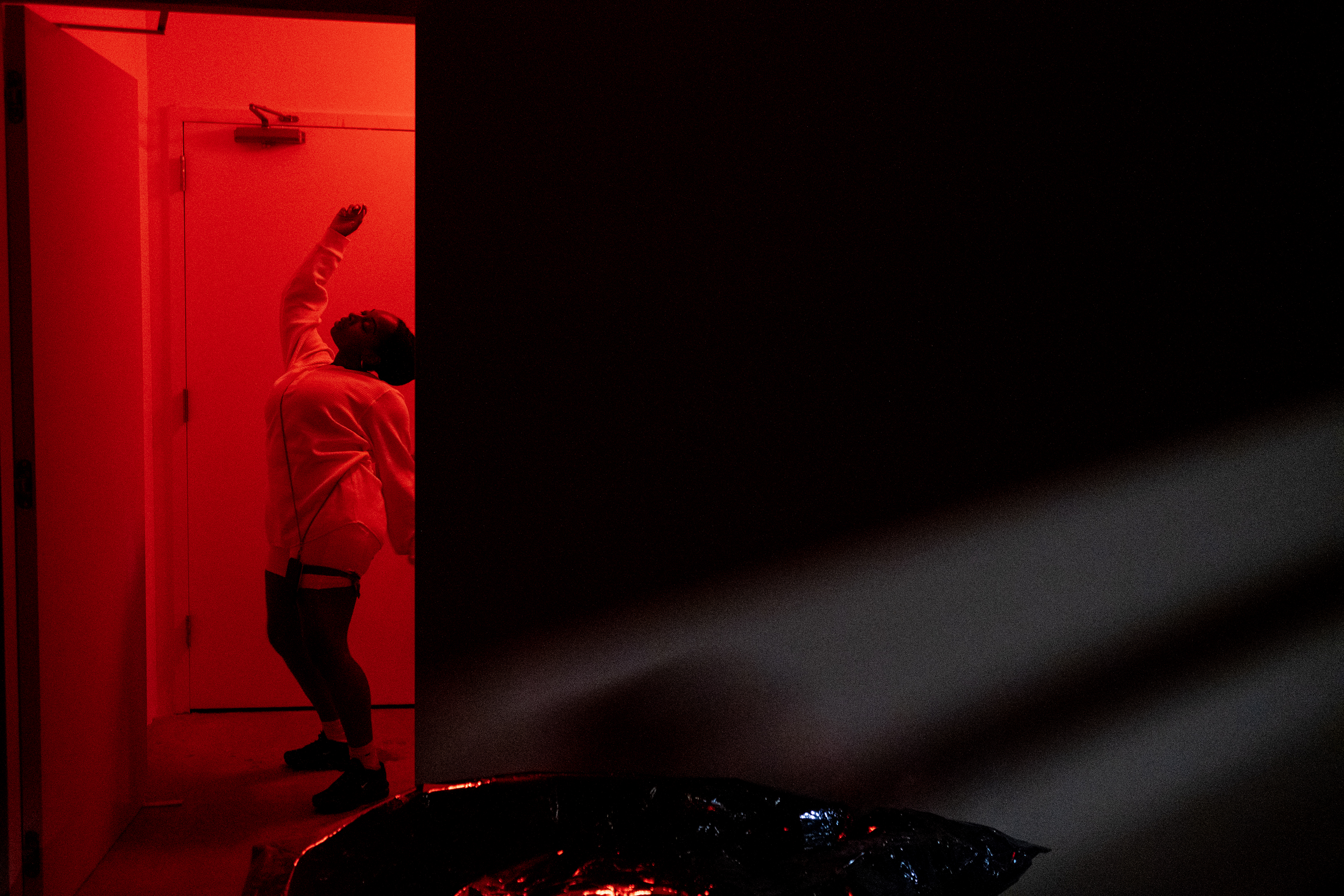 Color photograph of a figure dressed in all white, dancing in a corridor bathed in red light.