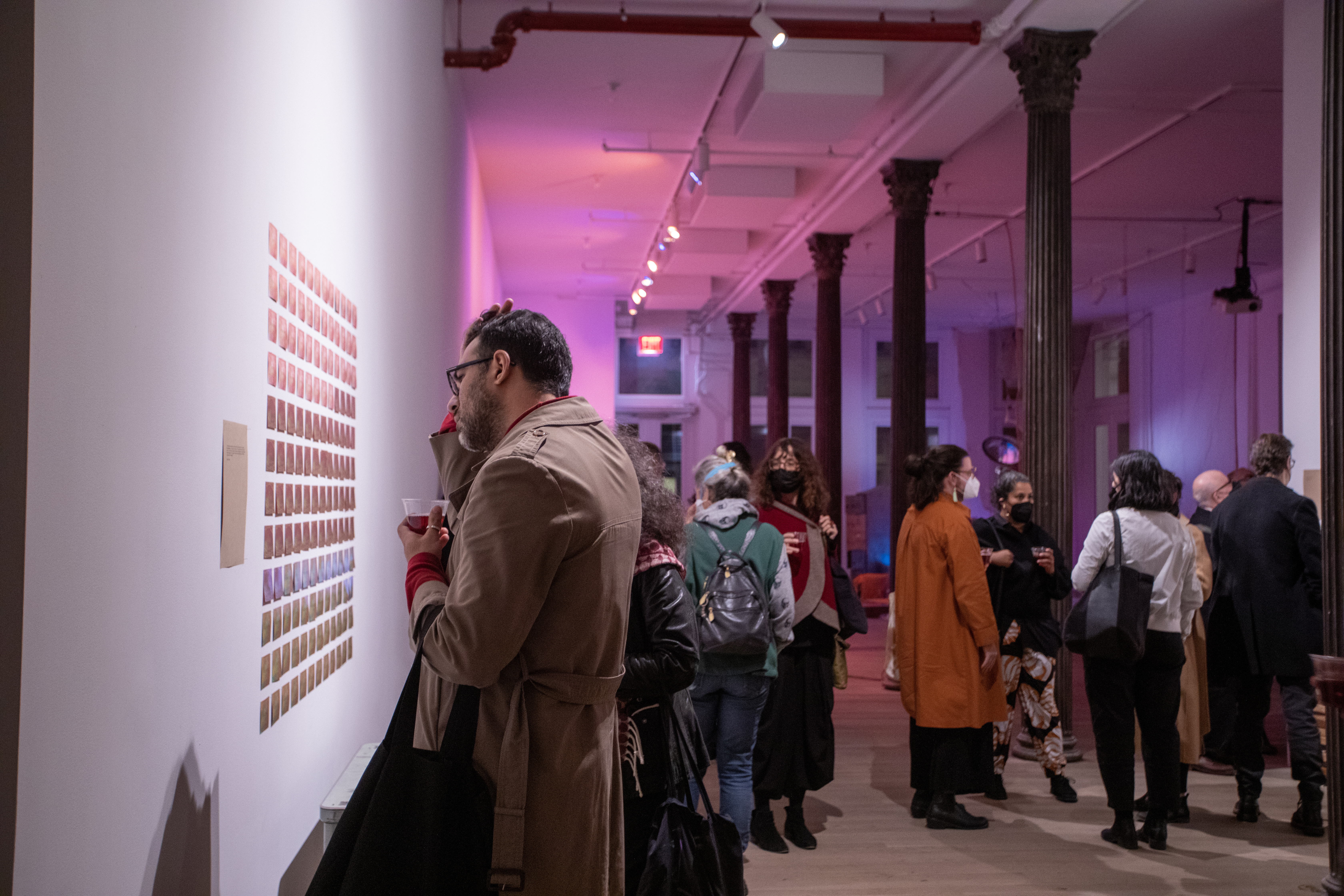 Color photograph of visitors standing around a gallery space, conversing and studying the works on the wall.