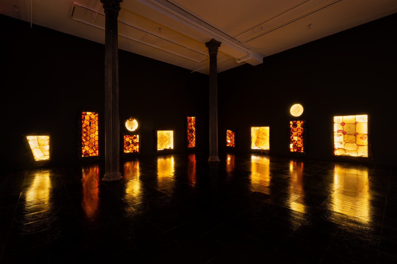 A color image of a dark room featuring illuminated yellow and orange shapes floating on the wall and reflected on the floor.