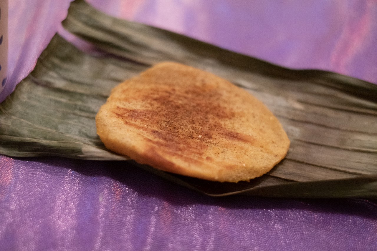 A color photograph of an arepa placed on a purple tablecloth.