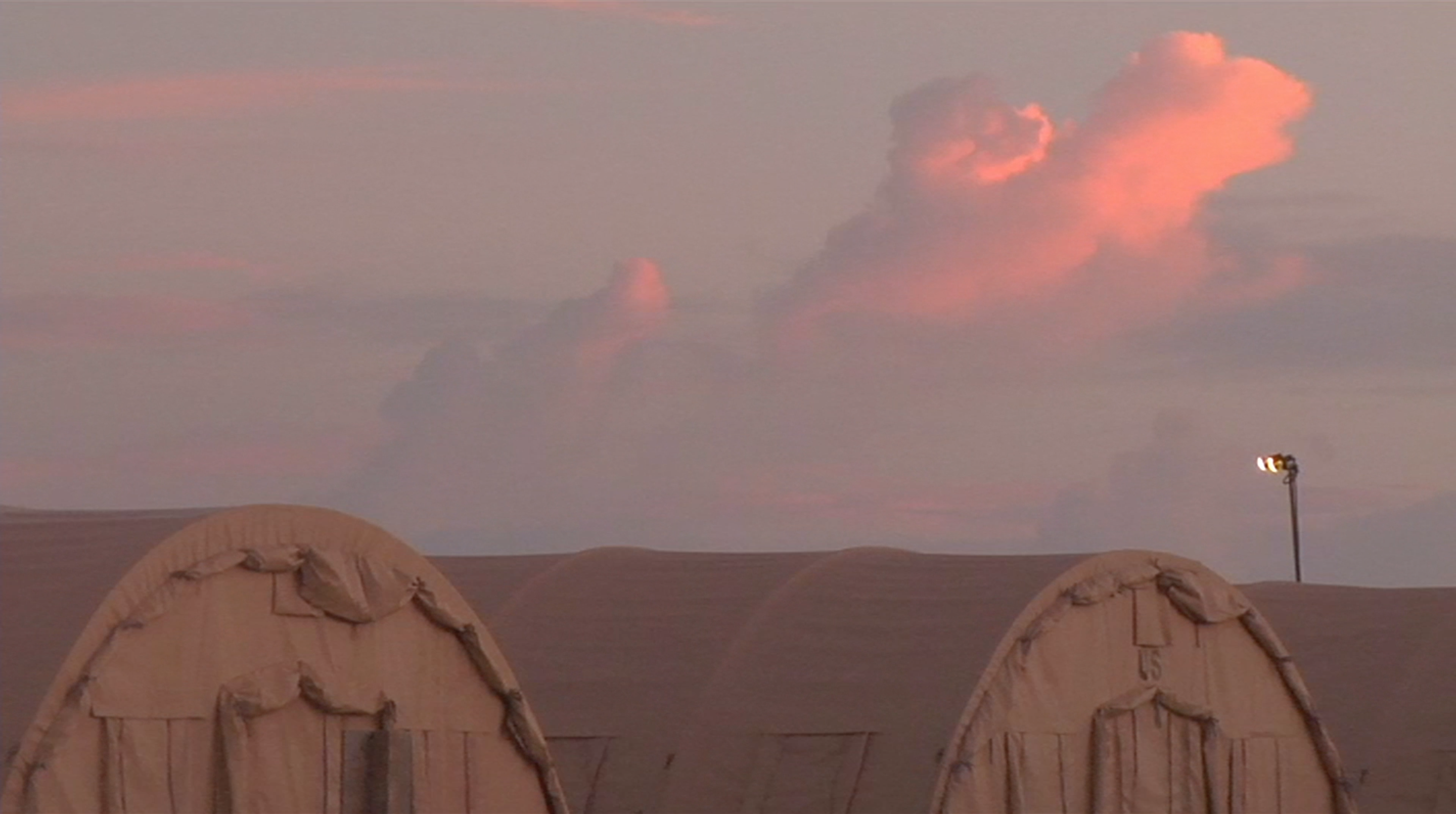 Foregrounded military tents with a pink sky in the background.