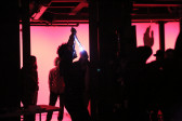 Several silhouetted figures backlit by a red glow stand among columns. The figure in the center holds a white-lit object in the air.
