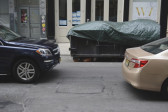 Two cars sitting on a city street in front of a dumpster covered with a tarp.