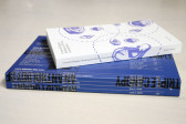 A white book lying on a larger blue book.
