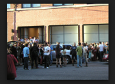 A crowd of people standing outside a brick building, mingling and talking.