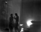 A black and white image of two blurry figures talking to each other in a dark room.