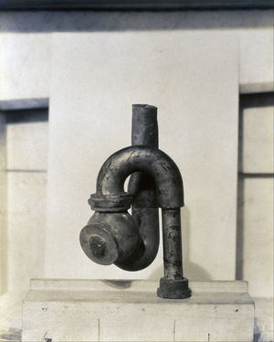 A black pipe coming out of a concrete slab beneath it, twisting around, pointed up and cut off, against a whitish slab behind it, as if to frame the pipe.