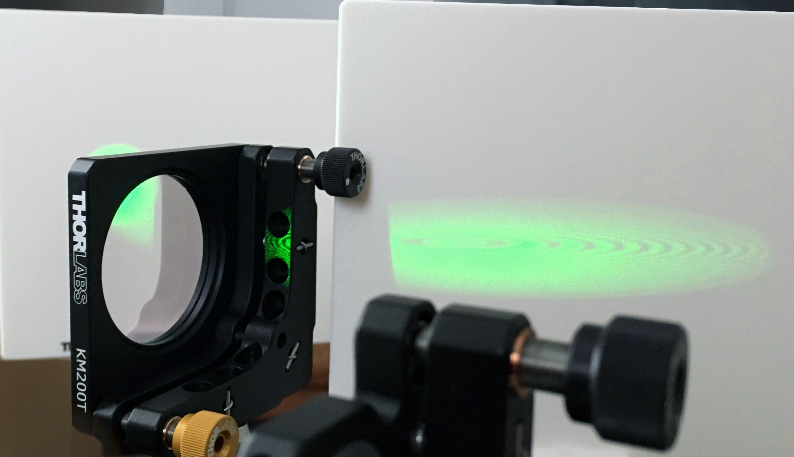 Detail view of an interferometer emitting a green light onto a white wall.