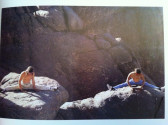 Two shirtless men doing the splits on top of large boulders outdoors.