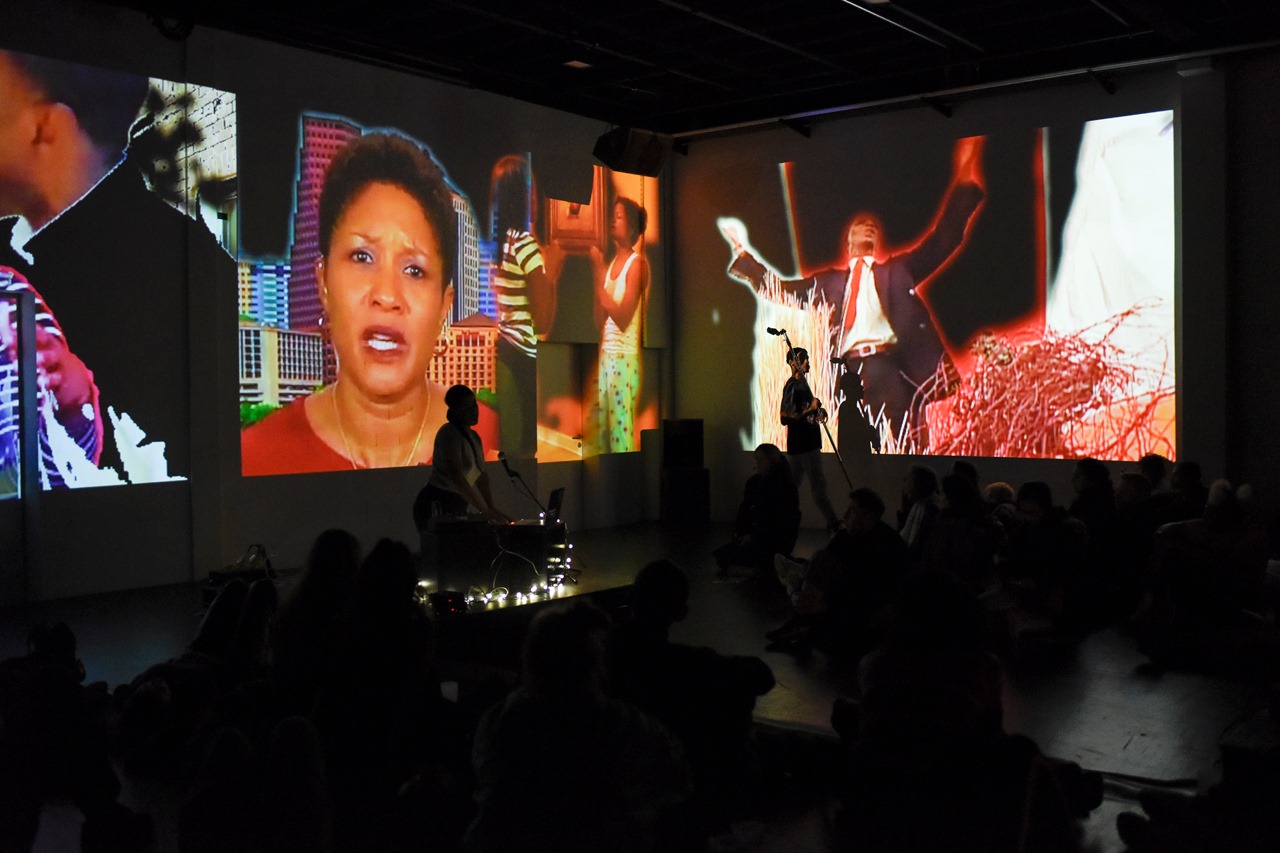 Two figures perform in front of large projected images.