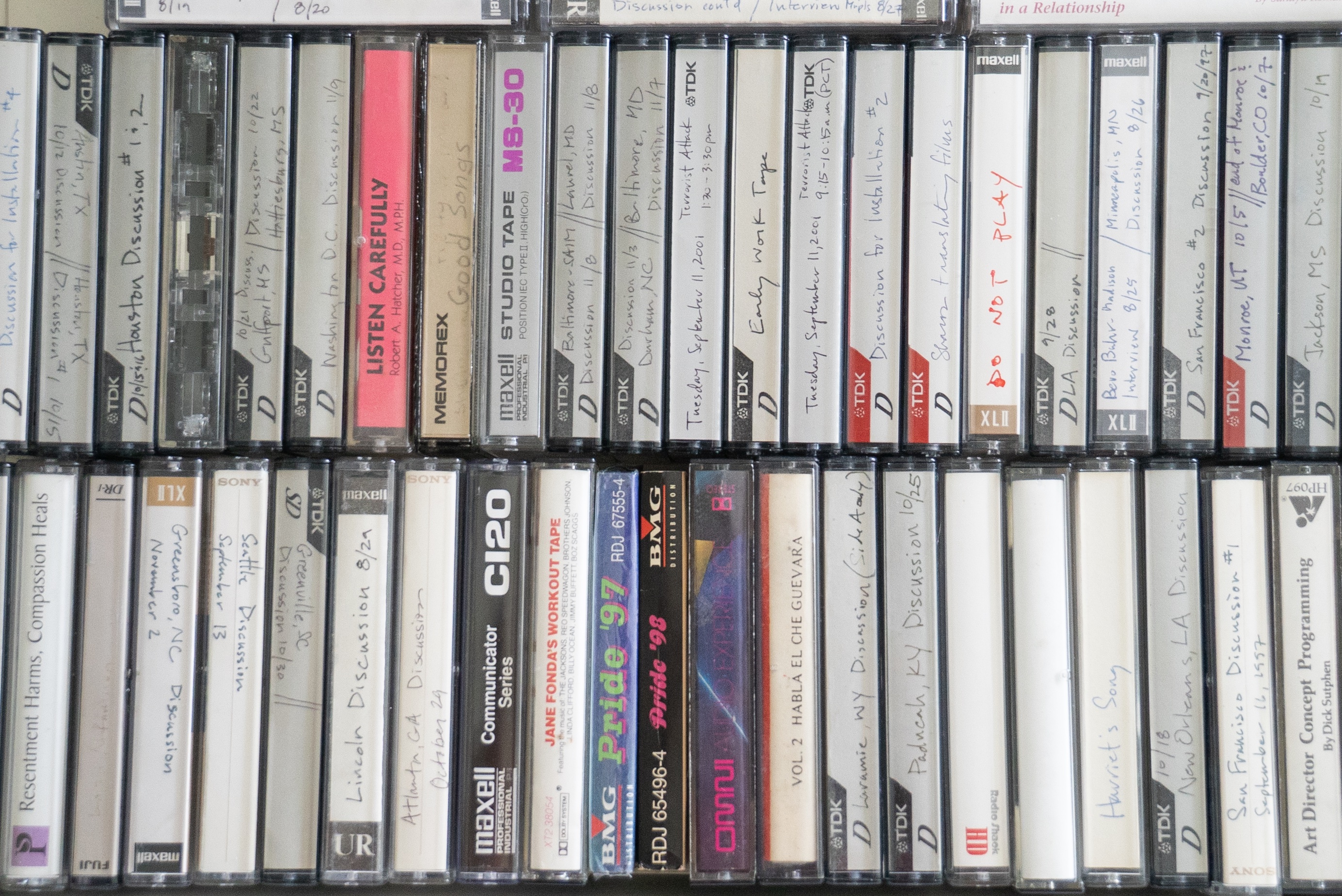 Rows of audio cassette tapes are tightly packed together. Many of the tapes have handwritten labels describing what is on the tape. 