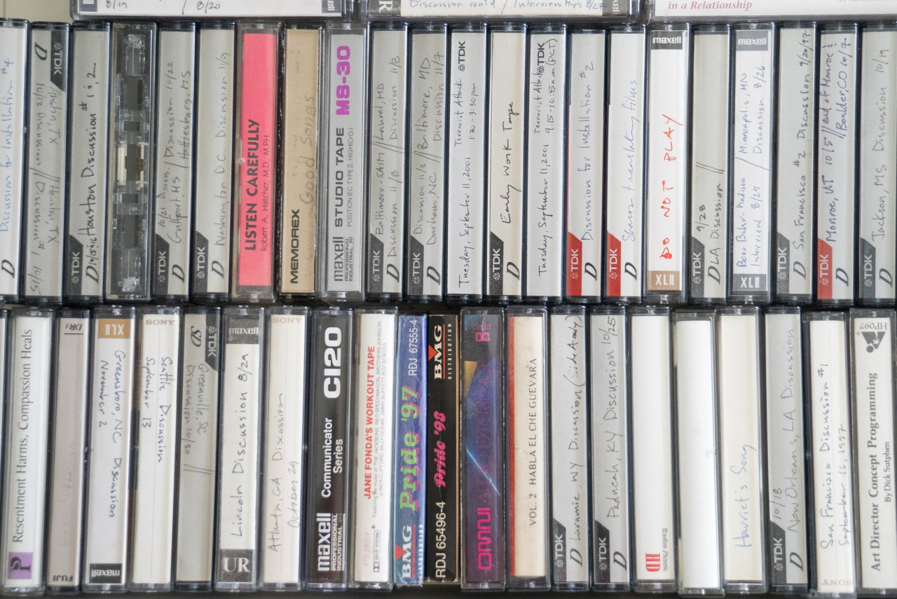 Rows of audio cassette tapes are tightly packed together. Many of the tapes have handwritten labels describing what is on the tape.