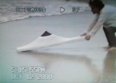 A VHS recording of a person holding an object on the beach.