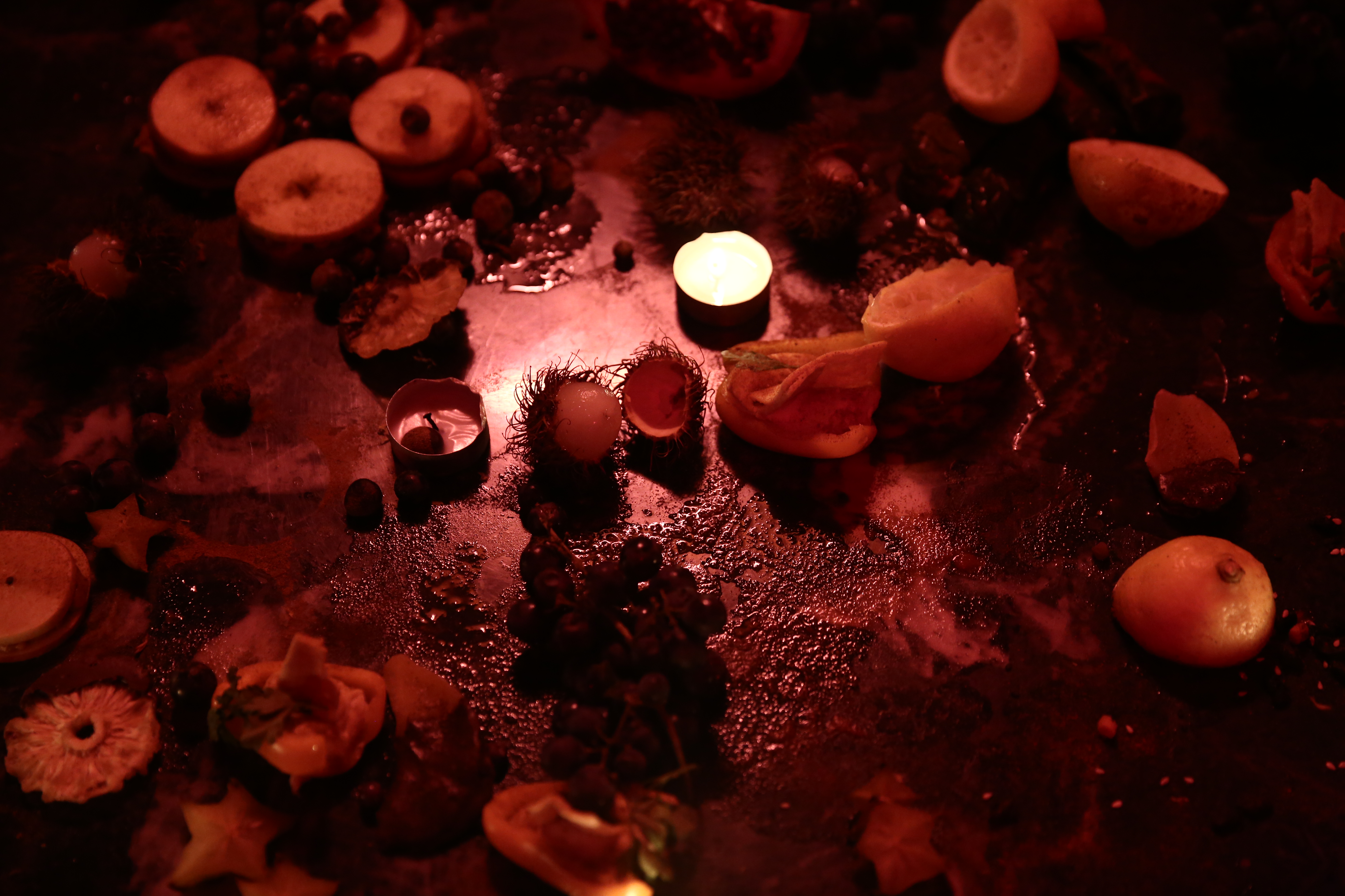 Half-eaten fruit, chocolate, and candles sit on a low, stone tabletop under dim lighting.