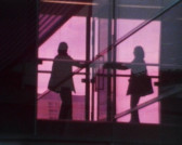A figure in dark, loose clothing pulls on a glass door, their mirror image reflected back through the glass. They are lit from behind by a pink glow.