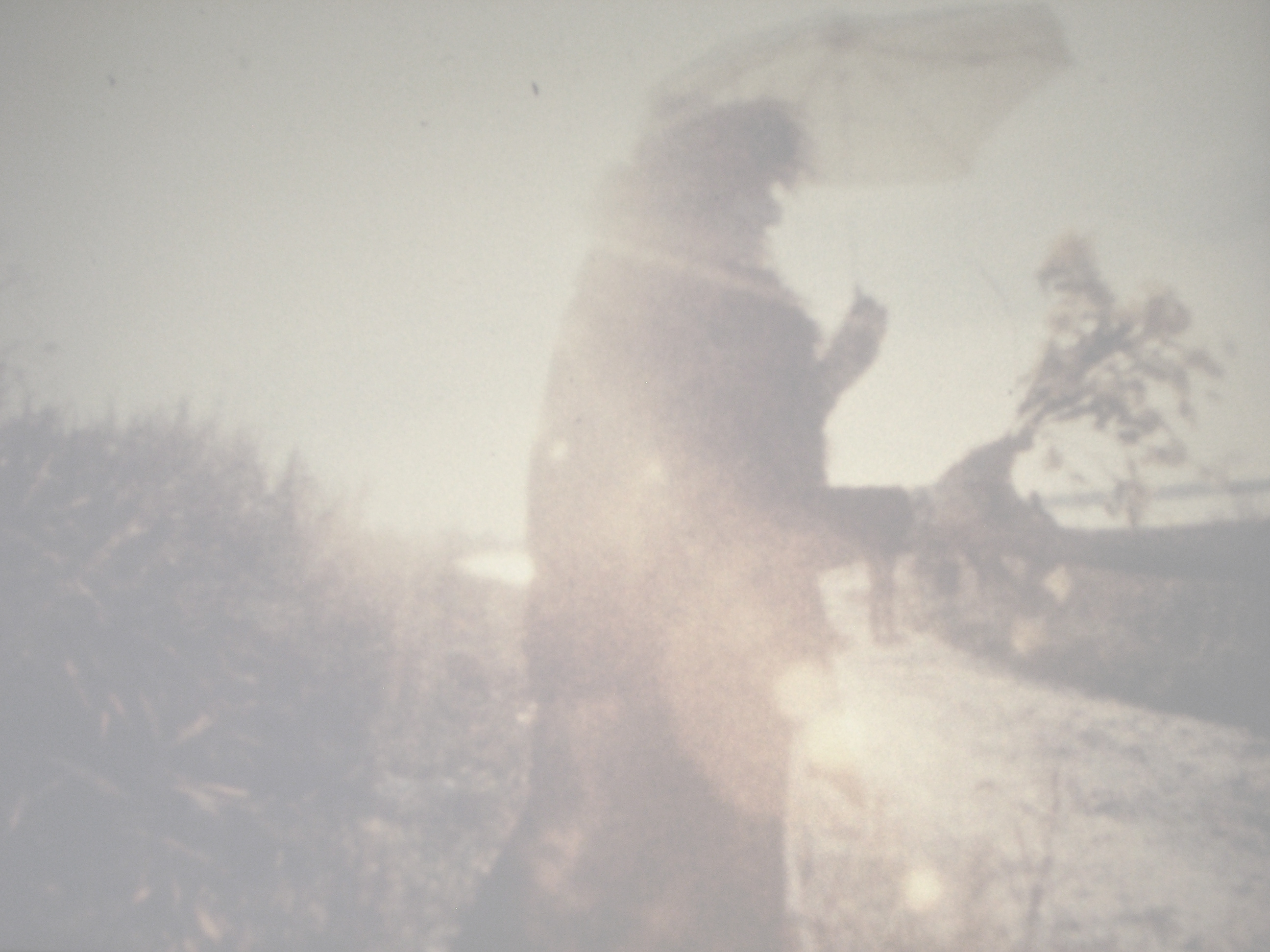 A faded image of a silhouette holding an umbrella outdoors
