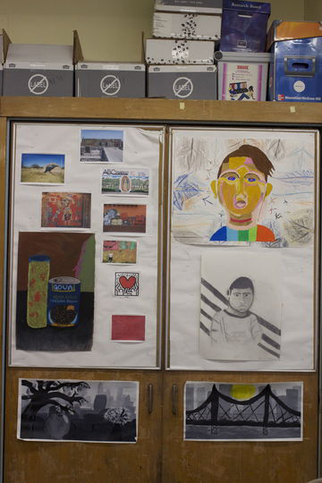 Several drawings and small paintings pinnned to the outside of a cabinet depicting city scenes, portraits, and still life images.