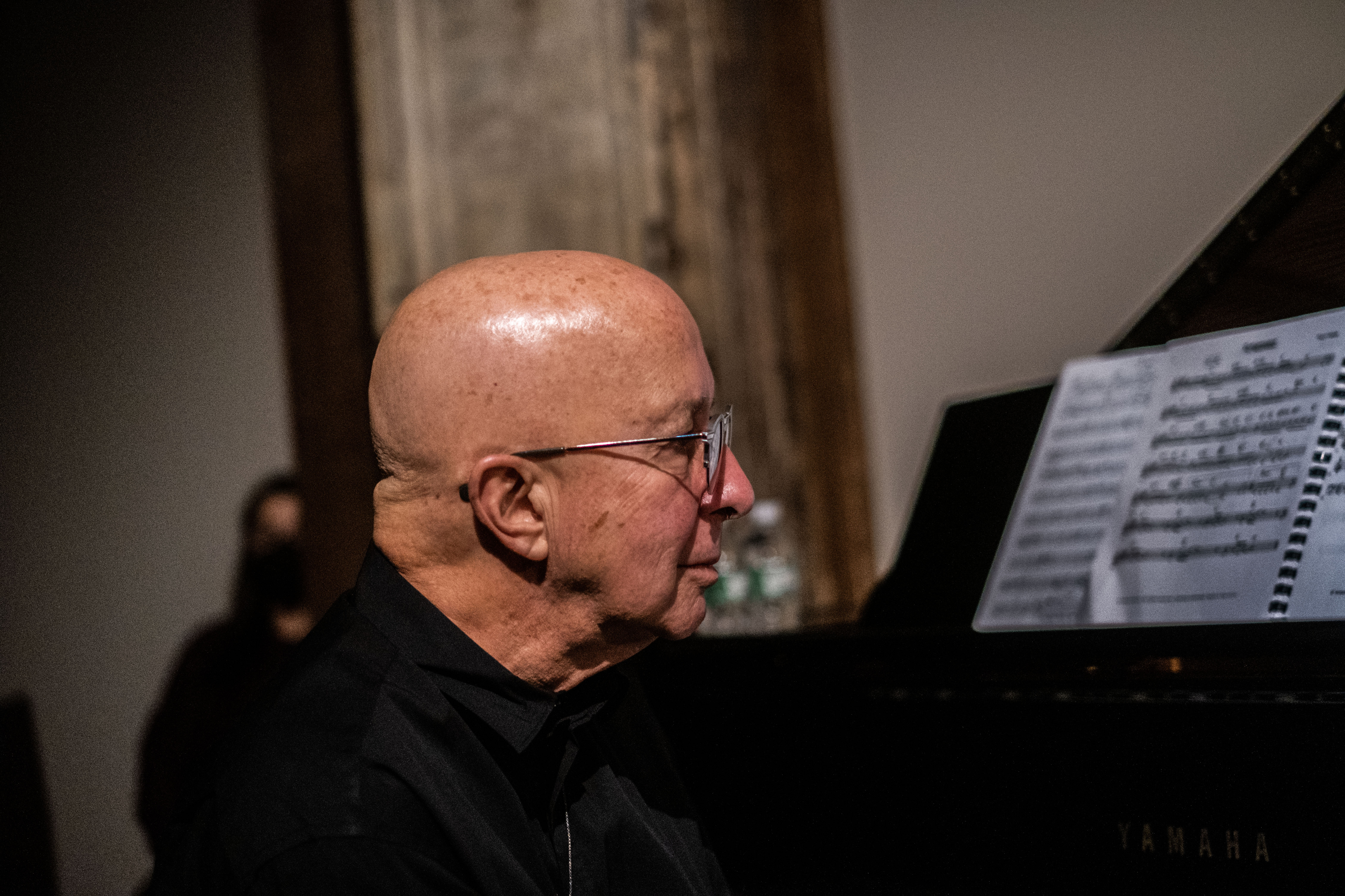 A figure in side profile studies sheet music placed on a piano.