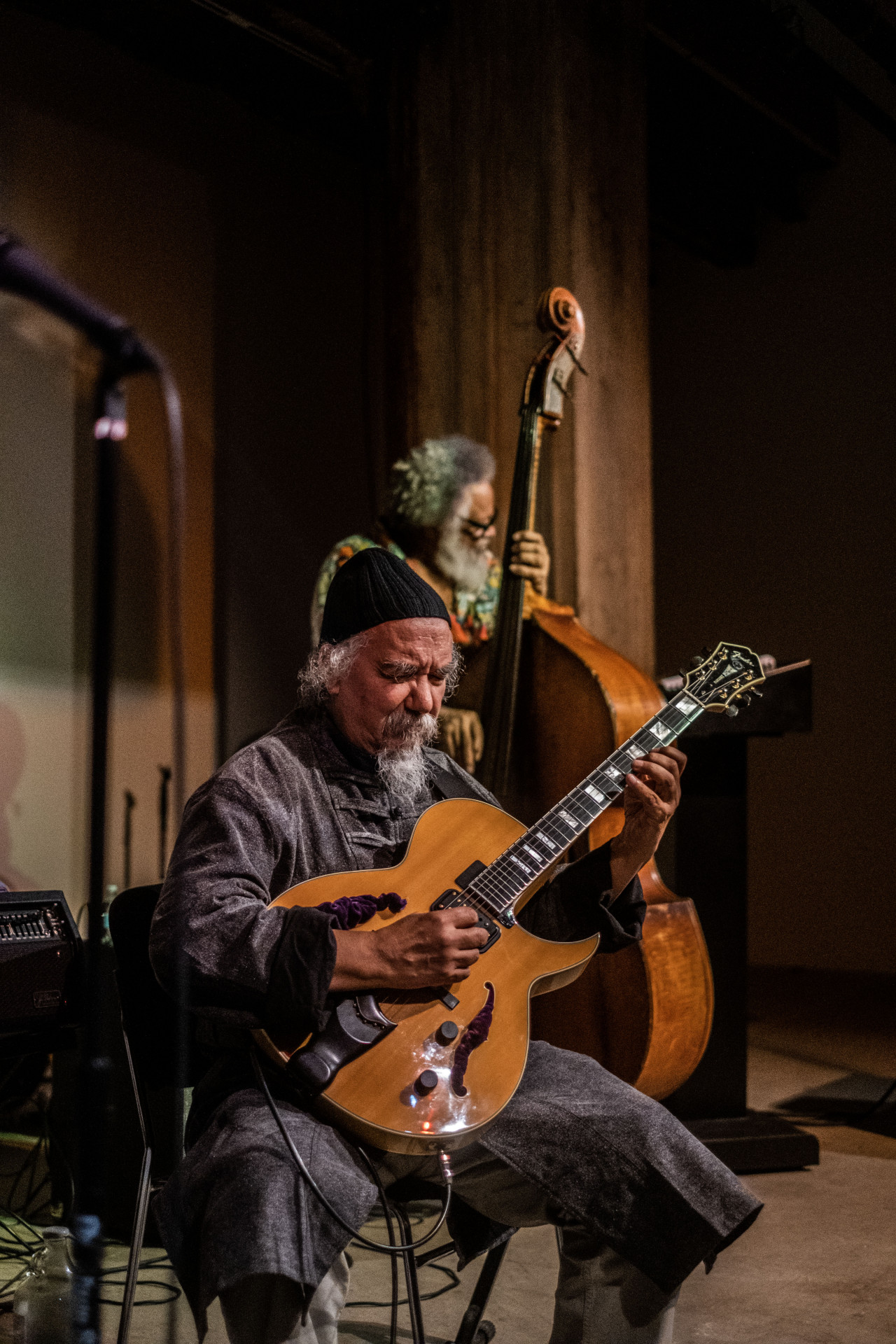A figure plays the guitar sitting down, while another figure stands behind him playing the bass.