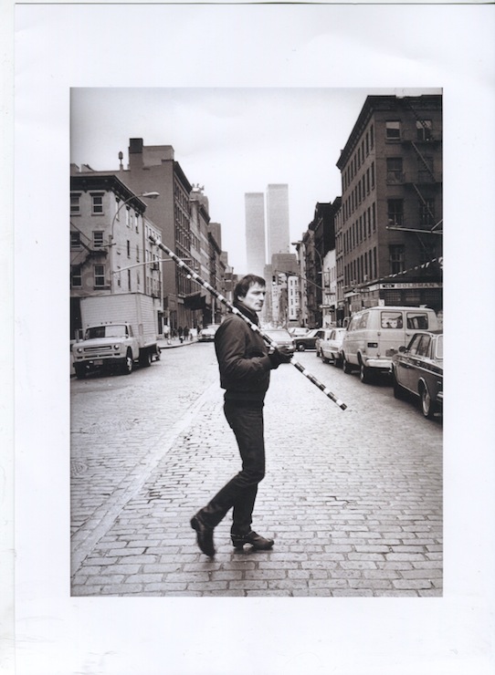 A black and white photo of a man standing on a cobblestone street in New York, with the Twin Towers in the background.