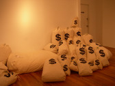 Roughly two dozen stuffed laundry bags, piled up against a wall. The bags are white and are each imprinted with a large black dollar sign.