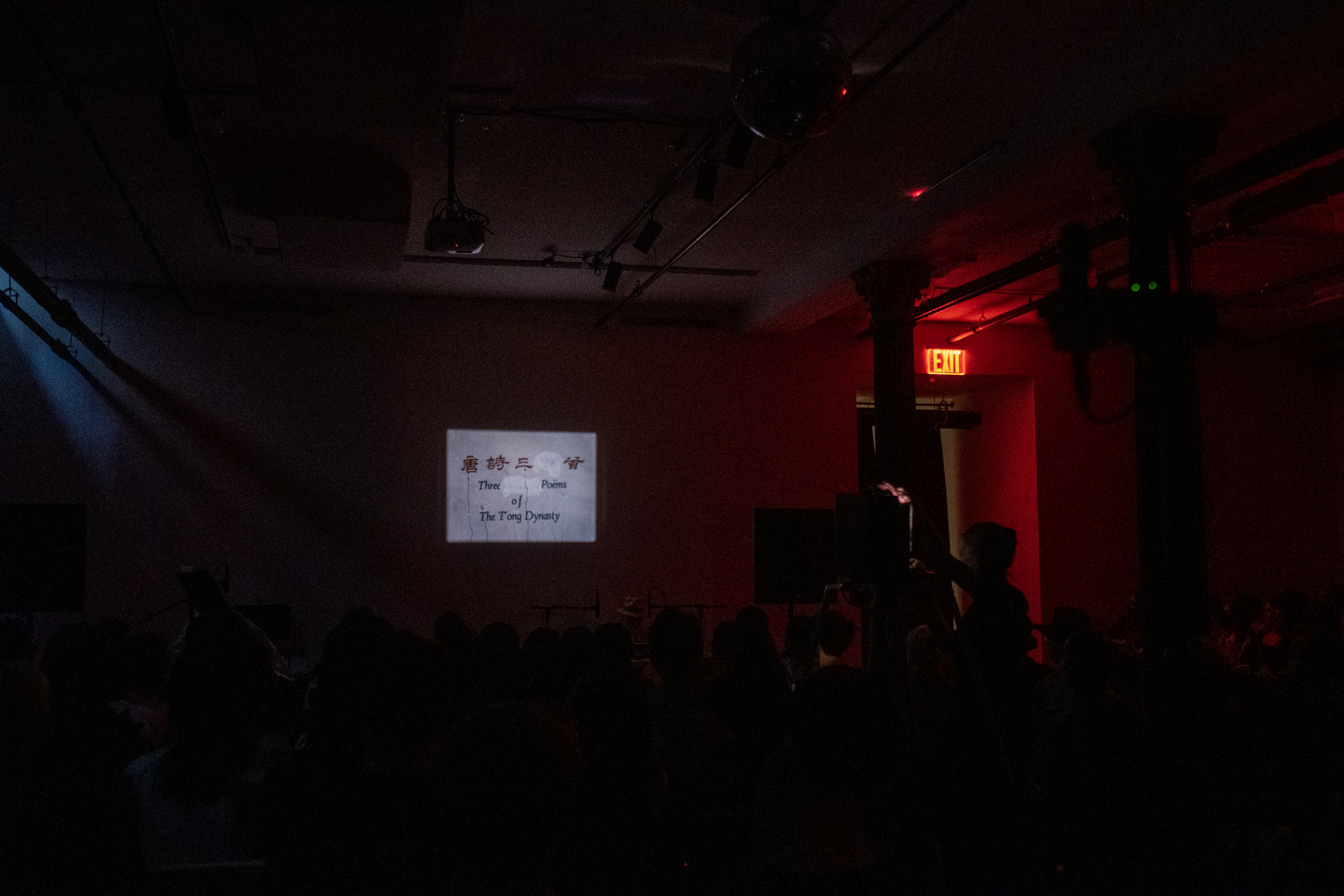 Color image of a dark basement room. On the back wall is projected an image with Chinese characters, and English characters that read 