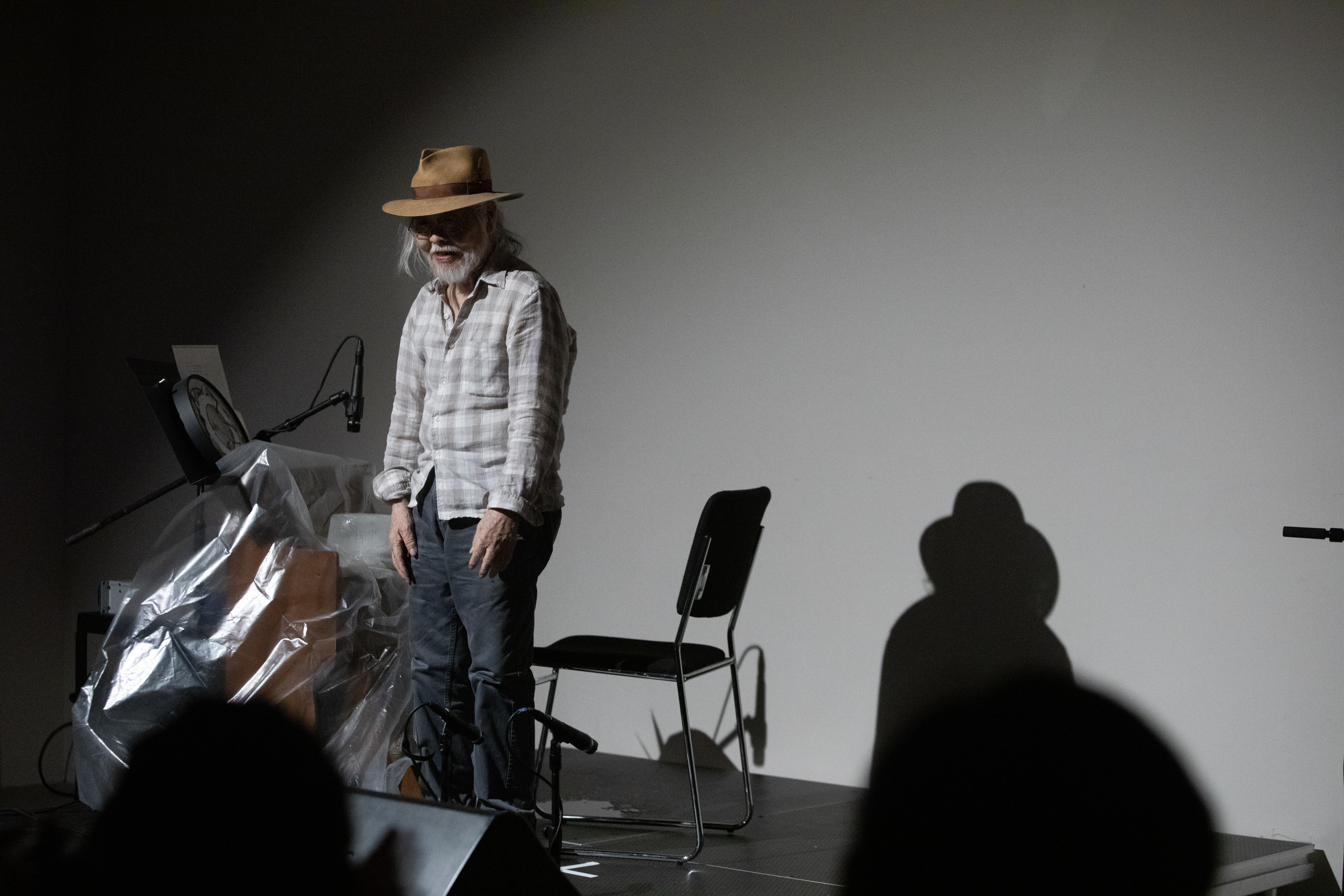 Color image of a figure standing on a black stage. They smile out at the audience as they prepare to perform in front of a reedorgan covered in plastic wrap.