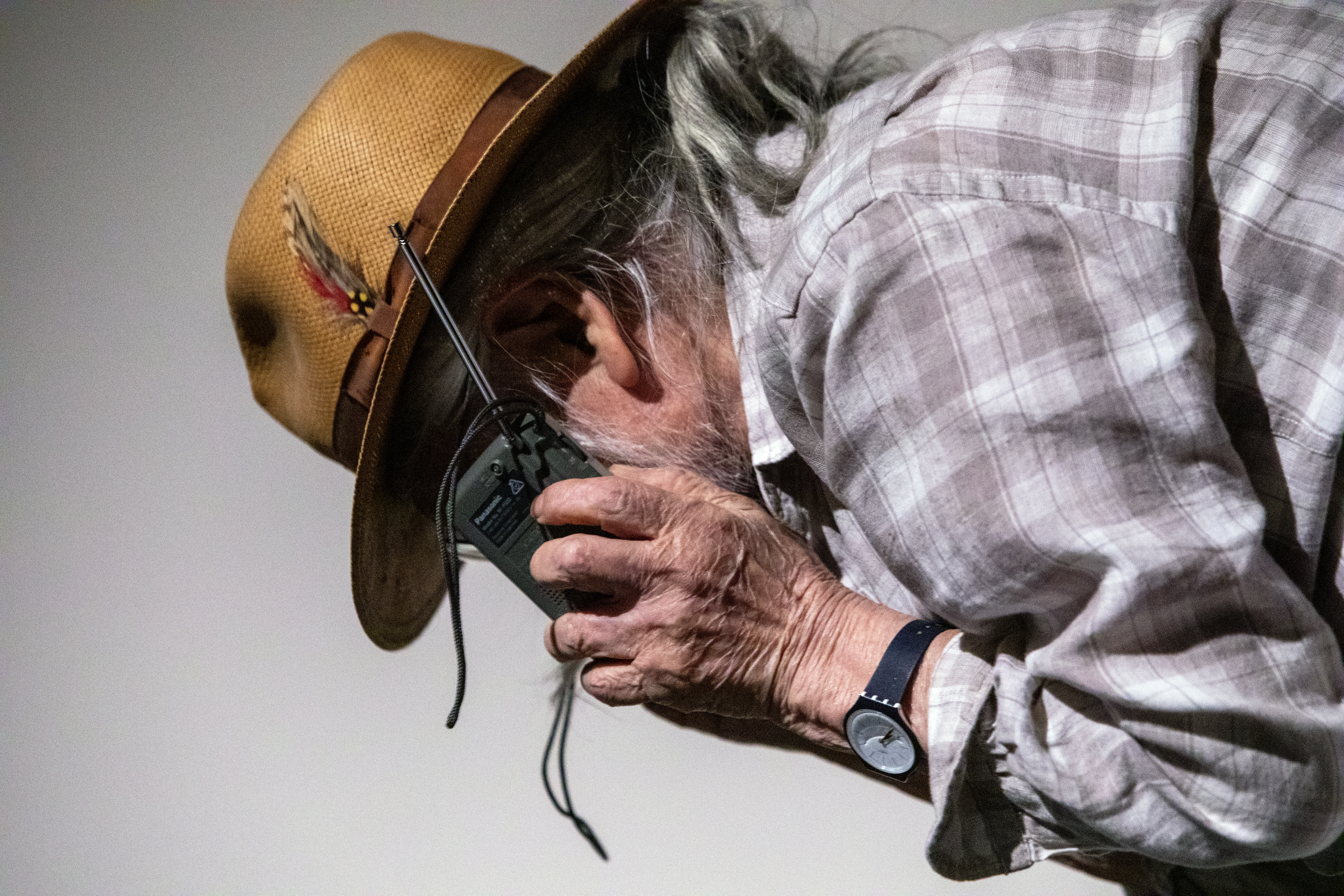 Color image of a closeup of a figure, in profile, holding up a small radio to their ear.