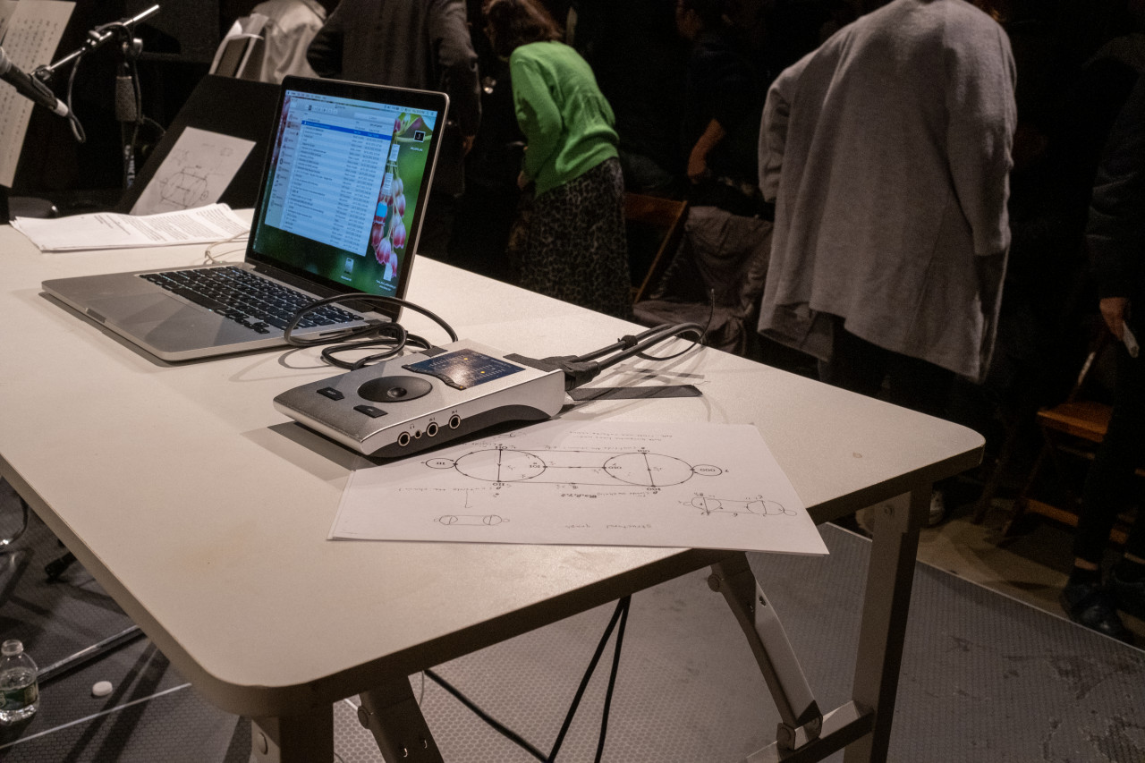 Image of a white desk on a black stage. Layed across the desk is a laptop and a control pad, along with a paper with printed instructions and diagrams.