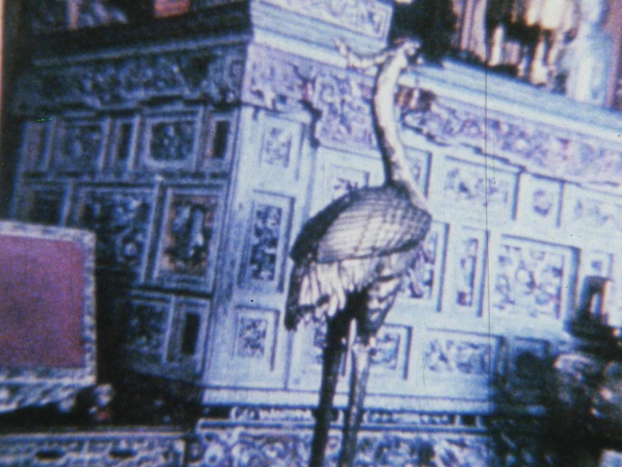 Color image of a bird sculpture placed in an ornately decorated room.